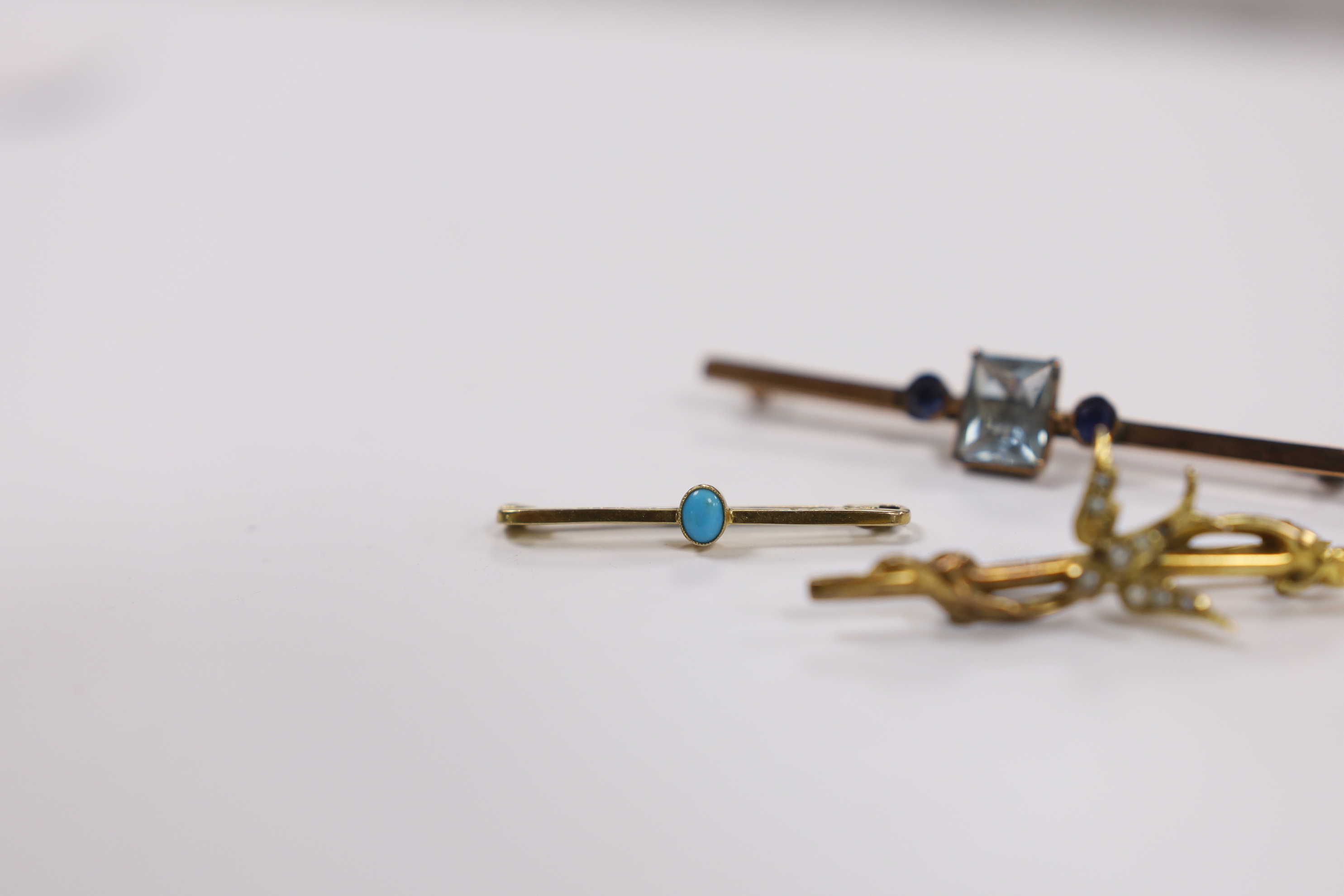 An Edwardian 9ct gold and seed pearl set swallow bar brooch, 43mm, a 9ct gold and turquoise set tie pin and a yellow metal, single stone aquamarine and two stone sapphire set bar brooch.